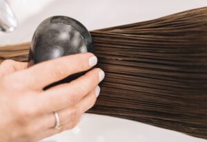 Close-up of a woman brushing long brown hair with a black brush, highlighting hair care and grooming.