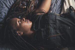 A contemplative woman with braided hair lying on a bed, expressing thoughtfulness.