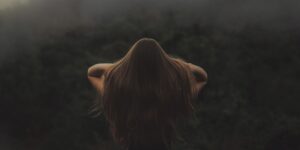 Back view of a woman with long hair, standing in a misty forest.