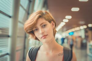 A confident young woman with short hair and piercings standing in a modern indoor setting.