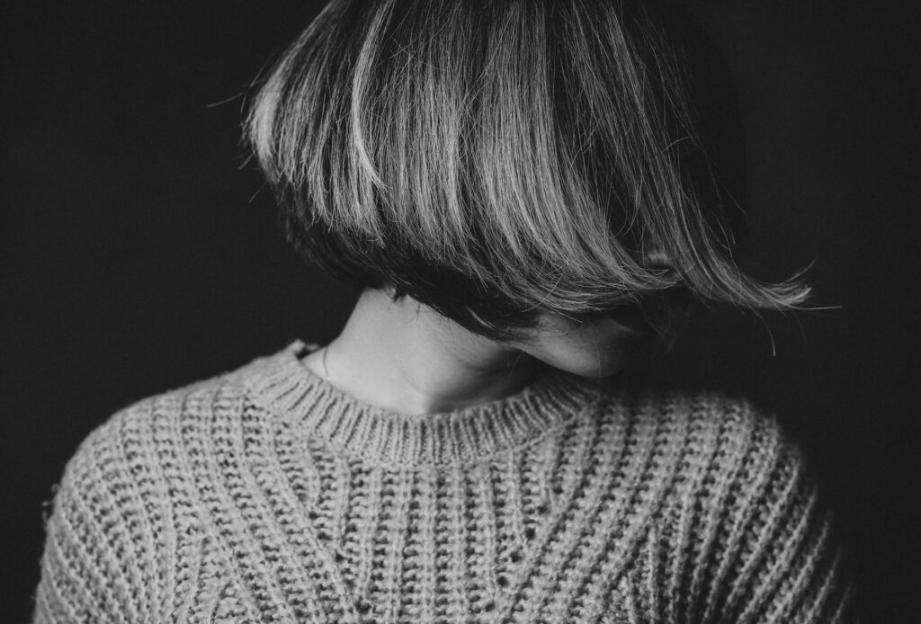 Striking black and white portrait of a woman with obscured face, wearing a textured sweater.