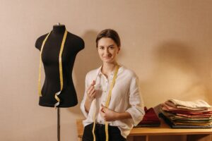 Smiling fashion designer with measuring tape and mannequin in cozy studio setting.